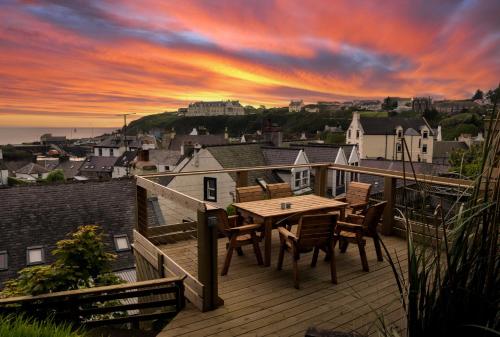 a deck with a wooden table and chairs at sunset at The Portpatrick Pad - A cosy 3 bed cottage, w. sea views & garden office in Portpatrick