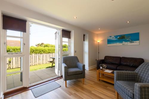 a living room with a couch and chairs and a sliding glass door at Bay Retreat Villas in Padstow