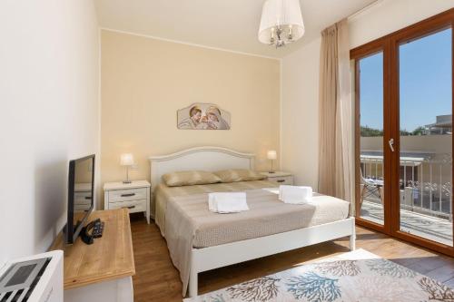 1 dormitorio con cama, TV y balcón en Il Sole en San Vito lo Capo