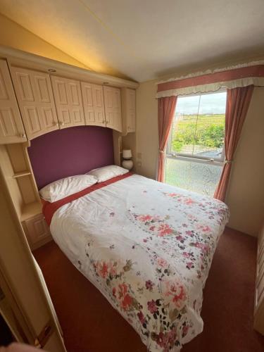 a bedroom with a bed with a floral bedspread and a window at Seaside Chalet in Quilty