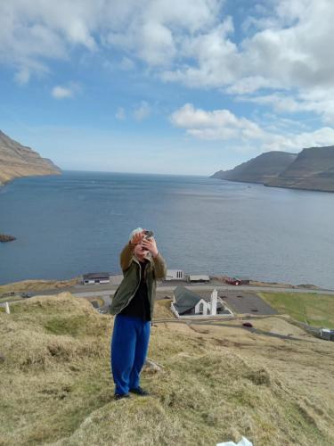 a woman standing on a hill taking a picture of the water at Experience unique Faroe Islands holiday home by the sea with great views, fully equipped kitchen and reliable Wi-Fi 