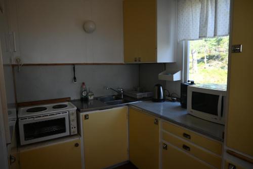 a small kitchen with yellow cabinets and a microwave at Rolfskärrs Stugby in Nygård
