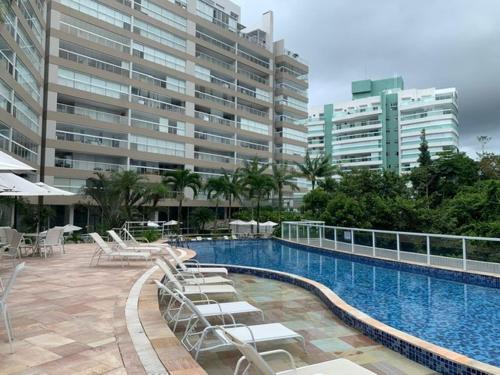a swimming pool with lounge chairs and a large building at Piscina Aquecida-Wifi-Net-Condomínio Reserva da Mata Módulo 8 Riviera de São Lourenço in Riviera de São Lourenço