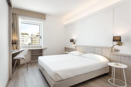 Biała sypialnia z łóżkiem, biurkiem i oknem w obiekcie Hotel Carlo Felice Sassari w mieście Sassari