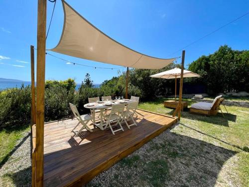 una terraza de madera con mesa, sillas y sombrilla en Maison en bord de mer en Coggia