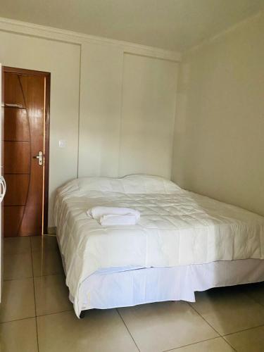 a white bed in a room with a wooden door at Hotel Santorine Prime - Itabira in Itabira