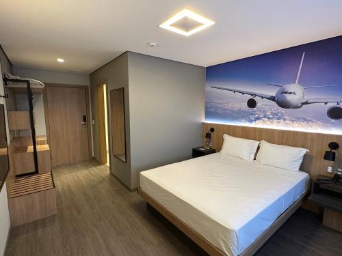 a bedroom with a bed with a plane painting on the wall at Hotel Panamby Guarulhos in Guarulhos