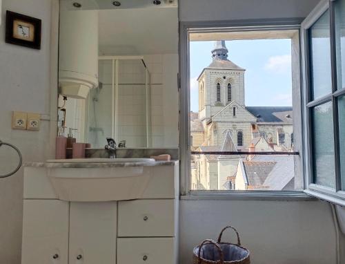a bathroom with a sink and a window with a church at T2 vue sur Loire local vélo in Saumur