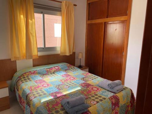 1 dormitorio con 1 cama colorida y 2 toallas en Seaside apartment with balcony, en Las Galletas