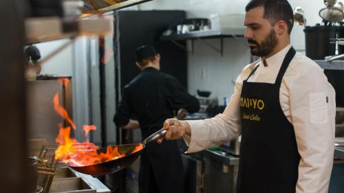 a man cooking food in a wok in a kitchen at Grand Mercure Curitiba Rayon in Curitiba