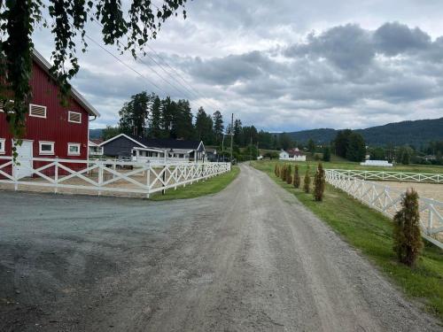a dirt road with a red barn and a white fence at Gårdsopphold Notodden in Notodden