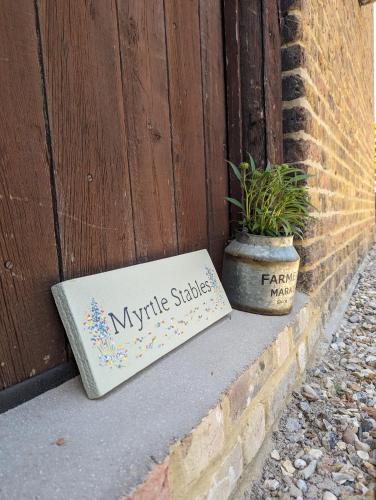 a sign sitting next to a wooden door with a potted plant at Myrtle Stables - converted, self-contained, countryside in Hernhill