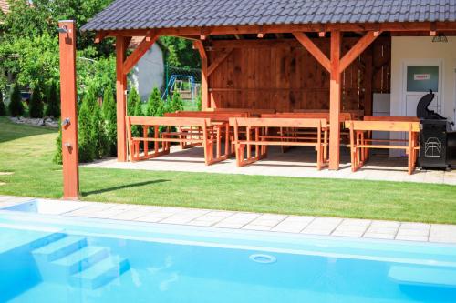 a wooden gazebo with a table and benches next to a pool at Rezidencia Podhájska in Podhájska