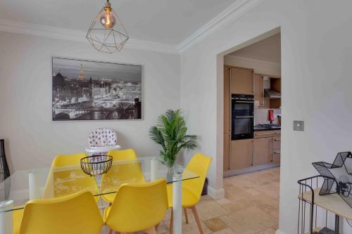 a dining room with a glass table and yellow chairs at Elizabeth II Five Bedroom Spacious Home in Bocking Churchstreet