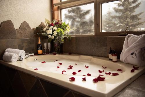 a bath tub with red rose petals on it at A Bear and Bison Country Inn in Canmore