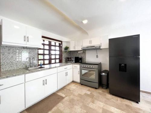 uma cozinha com armários brancos e um frigorífico preto em Beautiful Jungle House on a strategic location em Cancún