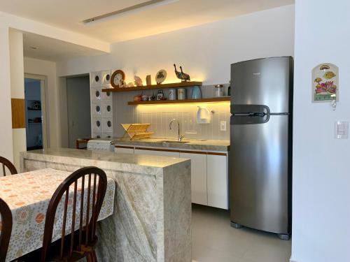 eine Küche mit einem Kühlschrank aus Edelstahl und einem Tisch in der Unterkunft Apartamento vista do mar, pé na areia e águas tranquilas, no cento de Guarapari in Guarapari