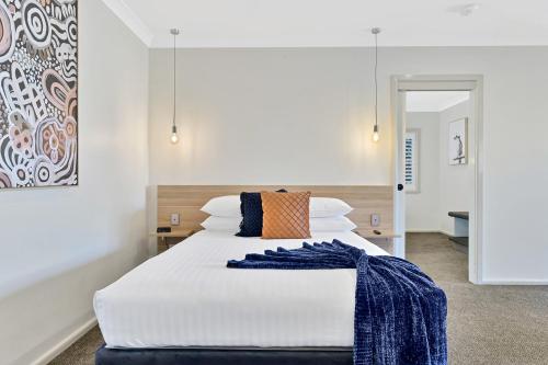 a large white bed with a blue blanket on it at Central Caleula Motor Lodge in Orange