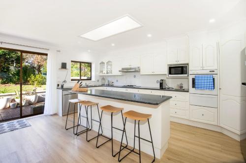 a kitchen with white cabinets and a island with bar stools at Seagrass Pet Friendly 10 Mins Walk to Beach in Vincentia