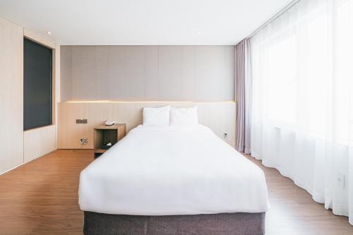 a large white bed in a room with a large window at The First70 Hotel in Seogwipo