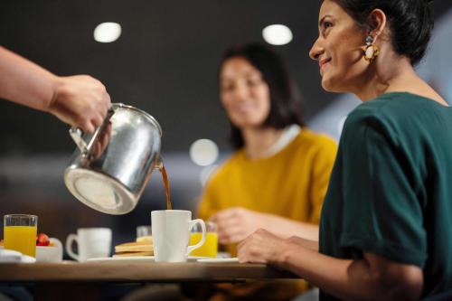 two women sitting at a table with a tea kettle at Holiday Inn Toledo - Maumee I-80/90 by IHG in Maumee
