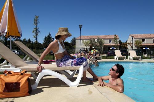 a woman sitting on a chair next to a man in a swimming pool at Résidence Odalys Les Sources de Manon in Vallon-Pont-dʼArc