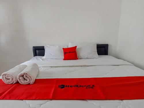a bed with a red pillow and towels on it at RedDoorz Syariah near RSUD Karawang 2 in Karawang