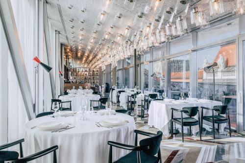 un restaurante con mesas y sillas blancas y ventanas en Met Boutique Hotel, en Zagreb