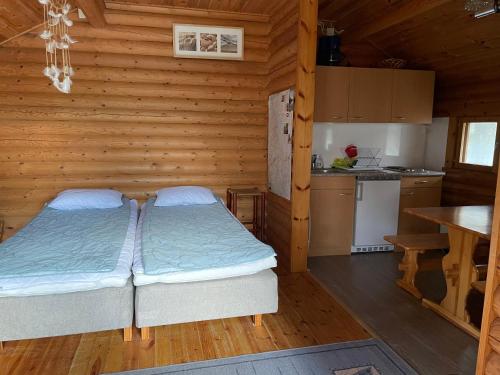 two beds in a wooden room with a kitchen at Kolmiloukon leirintäalue in Taivalkoski