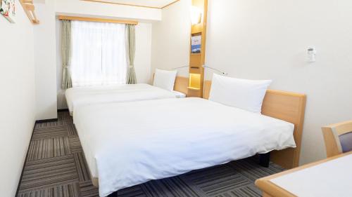 two beds in a hotel room with white sheets at Toyoko Inn Hokkaido Sapporo Susukino Junction in Sapporo