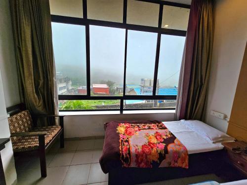 a bedroom with a large window and a bed and a chair at Suman Cottage & Bungalow in Mahabaleshwar