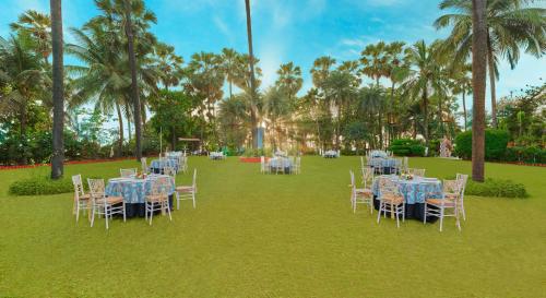 a group of tables and chairs on a lawn with palm trees at The Resort in Mumbai