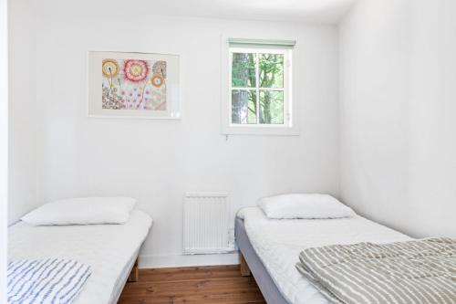 2 Betten in einem weißen Zimmer mit 2 Fenstern in der Unterkunft Fiskestugan – Country side cottage by lake in Sjöbo