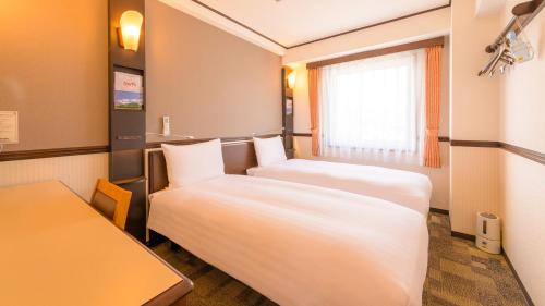 a room with two beds and a table and a window at Toyoko Inn Hon-atsugi-eki Minami-guchi in Atsugi