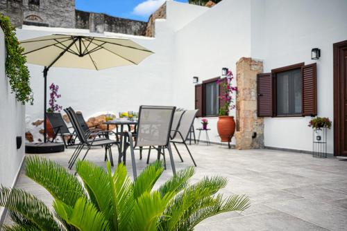 eine Terrasse mit einem Tisch, Stühlen und einem Sonnenschirm in der Unterkunft Villa Danae - Lindos in Lindos
