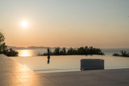 a person standing next to a white wall with the sunset at Villa Ekphrasis with sea view and jacuzzi in Ravdhoúkha