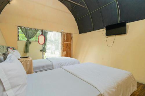 a bedroom with two beds and a tv and a window at Chikar Glamping At Wisata Coban Talun Mitra RedDoorz in Junggo