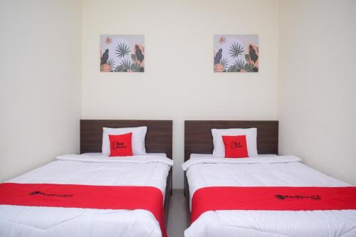 2 camas en una habitación con sábanas rojas y blancas en RedDoorz near Kawasan Bandara Ahmad Yani Semarang 2 en Kalibanteng-kidul