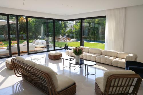 a living room with couches and tables and large windows at Breathtaking Villa w Pool & Sauna Near the Beach by Sea N' Rent in Herzliya