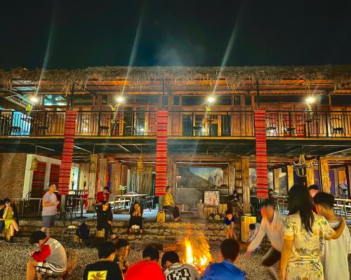 un grupo de personas sentadas alrededor de un fuego delante de un edificio en Moon Muong Sang House, 