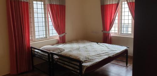 a bed in a room with two windows with red curtains at Signature Grande Villa, Kalathipady, Kottayam in Kottayam