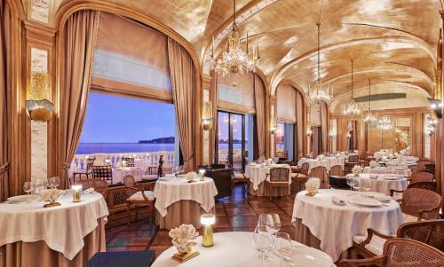 um restaurante com mesas e cadeiras brancas e uma grande janela em La Réserve de Beaulieu em Beaulieu-sur-Mer