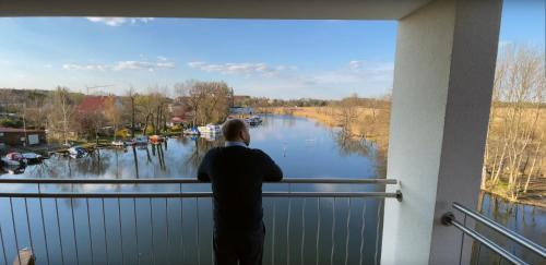 a man standing on a balcony looking out at a river at Havel-Spitze Ferienwohnungen in Brandenburg an der Havel