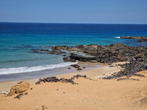 a sandy beach with rocks and the ocean at FUERTEVENTURAPARTMENTS in Corralejo