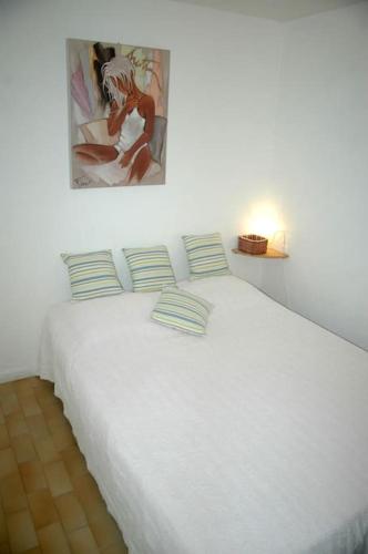 - un lit blanc avec des oreillers et un tableau mural dans l'établissement Appart 109, Port Soleil au village naturiste, au Cap d'Agde