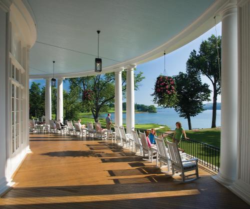 people sitting in chairs on a porch with a view of the water at The Otesaga Resort Hotel in Cooperstown
