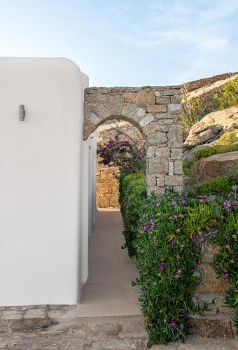 an entrance to a stone wall with flowers at Etesians Suites & Villas in Super Paradise Beach
