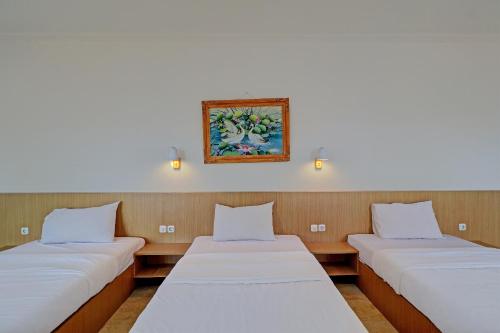 three beds in a room with a picture on the wall at Guest House Simalem in Legian