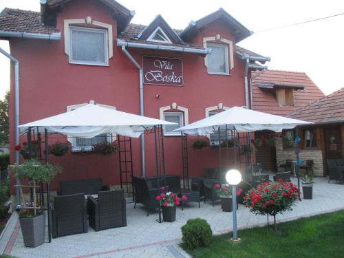 a restaurant with two umbrellas and chairs in front of a building at Vila Boska Palic in Palić