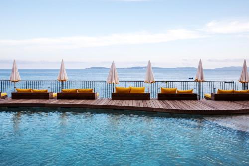 a swimming pool with couches and chairs next to the ocean at Hôtel Le Bailli De Suffren in Rayol-Canadel-sur-Mer
